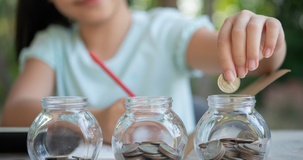 cute asian little girl playing with coins making stacks money kid saving money into piggy bank into glass jar child counting his saved coins children learning about future concept