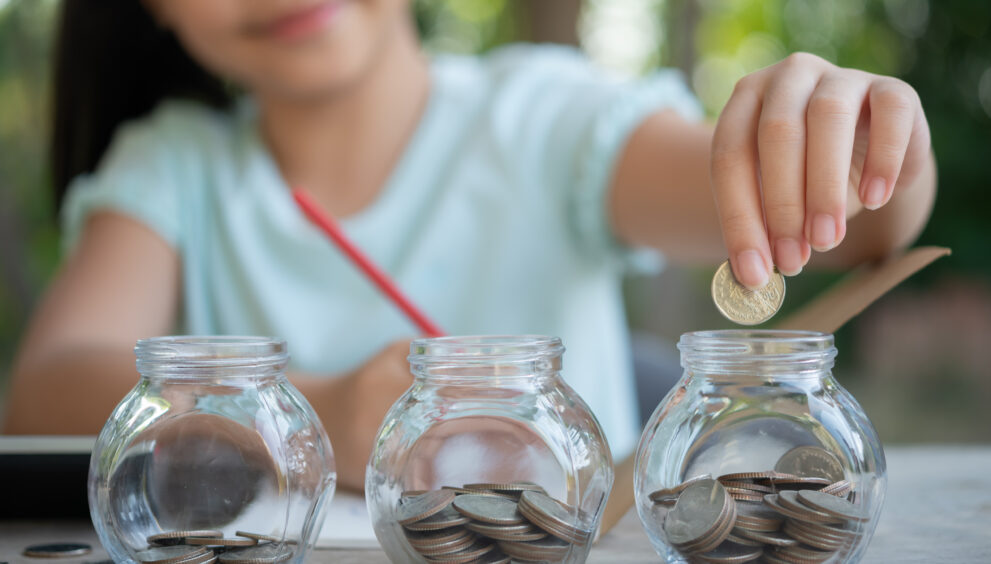 cute asian little girl playing with coins making stacks money kid saving money into piggy bank into glass jar child counting his saved coins children learning about future concept