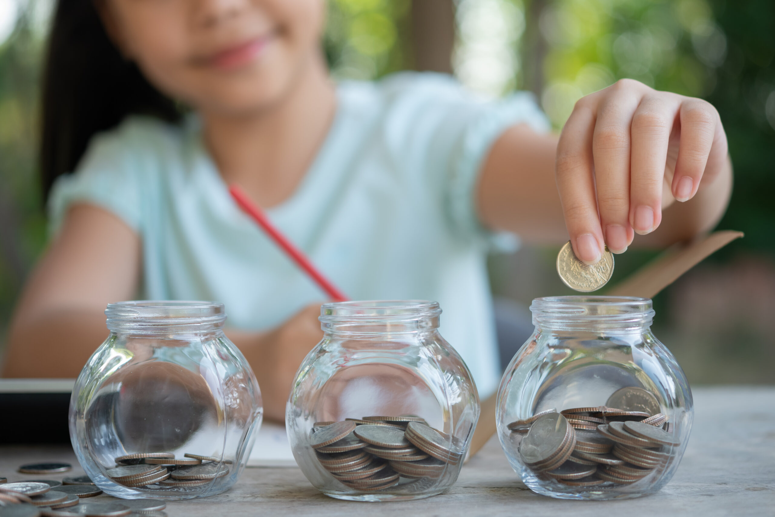 cute asian little girl playing with coins making stacks money kid saving money into piggy bank into glass jar child counting his saved coins children learning about future concept scaled